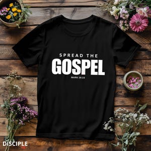 May include: A black short-sleeved t-shirt featuring white text that reads SPREAD THE GOSPEL and MARK 16:15. The shirt has a crew neckline and a standard fit, with the graphic printed in a bold, sans-serif font centered on the chest area.