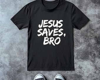 May include: A black short-sleeved t-shirt featuring the white text JESUS SAVES, BRO printed in a distressed, brush-stroke style on the chest. The shirt is displayed alongside a pair of black and white low-top canvas sneakers.