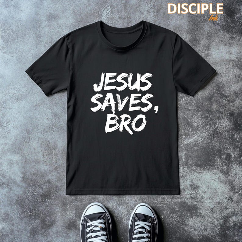Op de afbeelding: Zwart T-shirt met de witte tekst "JESUS SAVES, BRO". Het shirt wordt getoond op een grijze ondergrond, met een paar zwart-witte sneakers zichtbaar aan de onderkant van de afbeelding. De merknaam "DISCIPLE Ink" staat rechtsboven.
