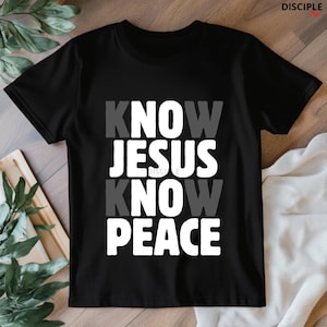 May include: Black t-shirt with the text "KNOW JESUS KNOW PEACE" in white and gray block letters. The shirt is a crew neck style and appears to be made of a soft material. The shirt is displayed on a light-colored surface.