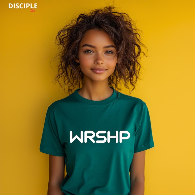May include: A woman wearing a green t-shirt with the word "WRSHP" printed in white on the front. She is standing in front of a yellow background.