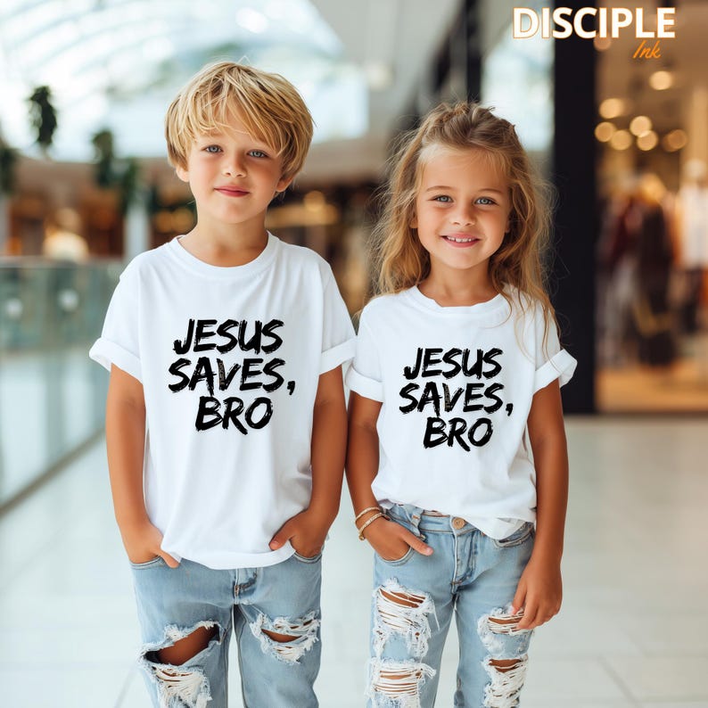 Op de afbeelding: Twee kinderen dragen witte t-shirts met de tekst "JESUS SAVES, BRO" in het zwart. Ze dragen ook een blauwe jeans. De afbeelding is goed belicht en de kinderen lachen.