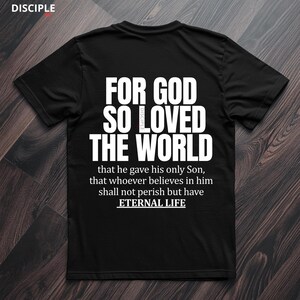 Pode incluir: Camiseta preta com texto branco: "FOR GOD SO LOVED THE WORLD" e um vers&iacute;culo b&iacute;blico. A camisa tamb&eacute;m tem a palavra "DISCIPLE" no topo. O texto continua com "that he gave his only Son, that whoever believes in him shall not perish but have ETERNAL LIFE."