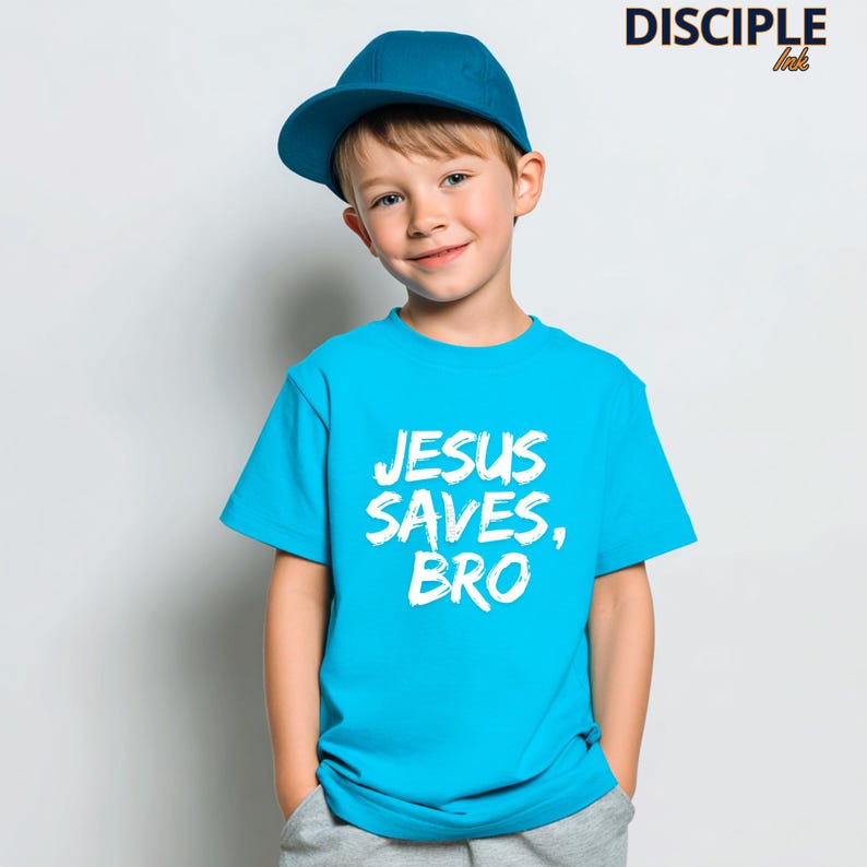 Op de afbeelding: Een kind draagt een turquoise t-shirt en een blauwe baseballpet. Het t-shirt toont de witte tekst "JESUS SAVES, BRO". De afbeelding bevat ook de tekst "DISCIPLE ink" in de rechterbovenhoek.