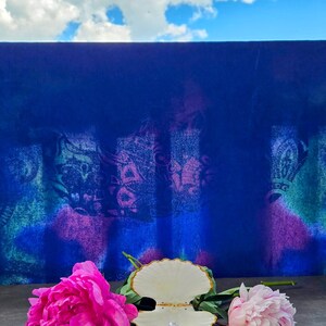 May include: A white seashell ring holder with a pearl ring inside, sitting on a grey surface with two pink peonies on either side. The background is a blue wall with a white cloud in the sky.