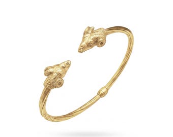 Puede incluir: Brazalete de puño dorado con detalles de cabeza de carnero en cada extremo. El diseño abierto facilita su uso. El brazalete tiene un diseño de cuerda trenzada y está sobre un fondo blanco.