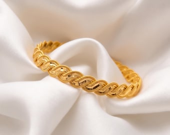 Puede incluir: Una pulsera rígida de oro con un patrón repetitivo de eslabones en forma de S. El metal tiene un acabado pulido y reflectante con detalles texturizados en los segmentos curvos, creando un diseño estructurado y entrelazado en toda la banda.
