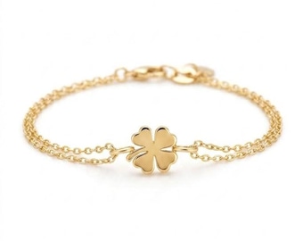 Puede incluir: Una pulsera de tono dorado con un diseño de cadena doble delicada. En el centro de la pulsera hay un dije pulido en forma de trébol de cuatro hojas. La pieza incluye un pequeño mecanismo de cierre circular en la parte posterior de la pulsera.