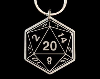 May include: A silver-colored D20 die keychain. The die is a twenty-sided polygon with numbers from 1 to 20. The number 20 is prominently displayed in the center. The keychain has a silver ring for attachment.