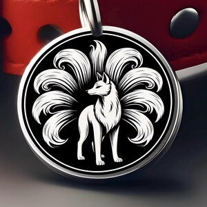 May include: A round, silver pendant featuring a white fox with nine tails against a black background. The fox is standing, facing left, with detailed fur. The pendant is attached to a silver loop, with a red leather collar in the background.