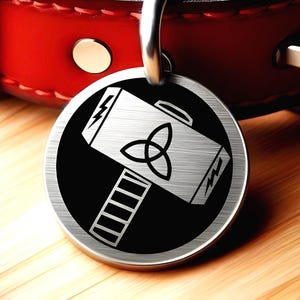 May include: A round, silver pet tag with a black background featuring a white hammer design with a triquetra symbol and lightning bolts. The tag is attached to a red leather collar with a silver clasp.