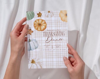 May include: Thanksgiving dinner invitation featuring watercolor pumpkins and fall leaves on a plaid background. The invitation text reads "Thanksgiving Dinner" with date, time, and address details. Held by hands against a white backdrop.