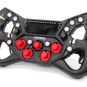 Puede incluir: Un volante de carreras negro Moza Racing para simulación, con una pantalla digital central, múltiples botones blancos, cinco diales giratorios rojos y codificadores de pulgar dorados etiquetados como TC, DIFF, BB y ABS.