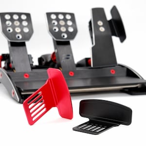 Könnte beinhalten: Ein schwarzes und graues Rennsimulator-Pedalset mit drei Pedalen, roten Akzenten und einer separaten roten und schwarzen Komponente. Die Pedale haben eine strukturierte Oberfläche mit mehreren Löchern. Für Sim-Racing-Enthusiasten.