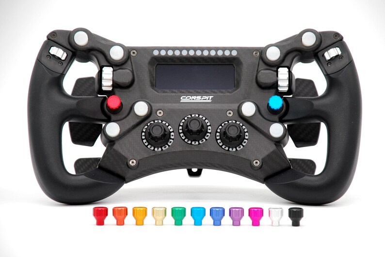 Peut inclure: Un volant de course sim en fibre de carbone noire avec un &eacute;cran num&eacute;rique central, plusieurs boutons, des cadrans rotatifs et des palettes de changement de vitesse. La marque CORSPIT est imprim&eacute;e en blanc. Onze petits boutons color&eacute;s sont en dessous.