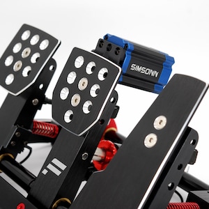 May include: Close-up of a black and silver racing pedal set with the brand name "SIMSONN" in white and blue. The pedals have a textured surface with multiple holes and silver accents. Red springs are visible.