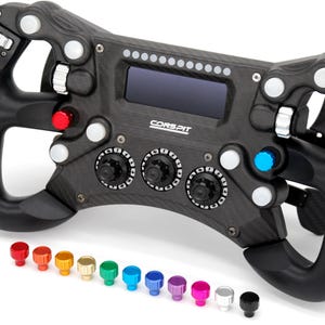 Puede incluir: Un volante de carreras de fibra de carbono negra con una pantalla digital central, varios botones plateados, rojos y azules, y tres diales giratorios. La marca CONSPIT está impresa en blanco. Once pequeños pomos de repuesto coloridos están alineados.