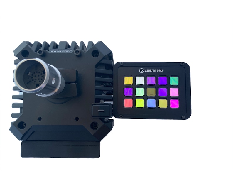 May include: A black Fanatec racing wheel base with a silver connector and a Stream Deck with multi-colored illuminated buttons. The Stream Deck is attached to the side of the wheel base.