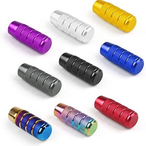 May include: Assortment of ten different colored shift knobs. The knobs are made of metal and have a ridged design. The colors include purple, silver, gold, blue, black, gray, red, and a rainbow iridescent finish.