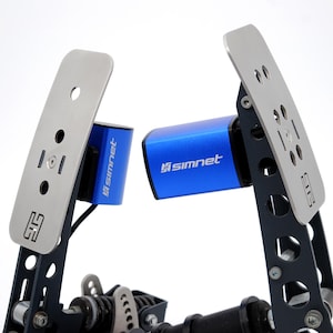 May include: A close-up of a racing simulator pedal set. The set features two silver pedals with multiple holes and a blue cylinder with the text "simnet". The pedals are mounted on a black frame.