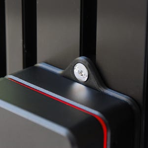 May include: A black 3D-printed mounting bracket attached to a vertical black aluminium extrusion rail. The bracket features a central circular opening with a silver metal fastener secured inside, and a thin red accent line along the top edge.