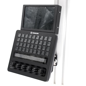 Puede incluir: Una consola de control Stream Deck negra con una pantalla superior, una cuadrícula de treinta y dos botones cuadrados, una banda táctil horizontal y cinco perillas giratorias circulares en la parte inferior, montada en un riel de soporte metálico plateado.