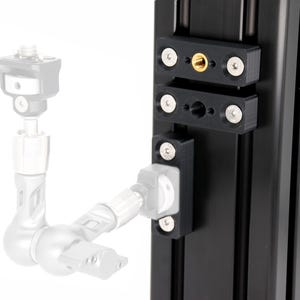 May include: Black metal camera mounting hardware with silver screws and a gold-colored threaded insert. The hardware is attached to a black vertical rail, with a partially visible camera mount and articulating arm.
