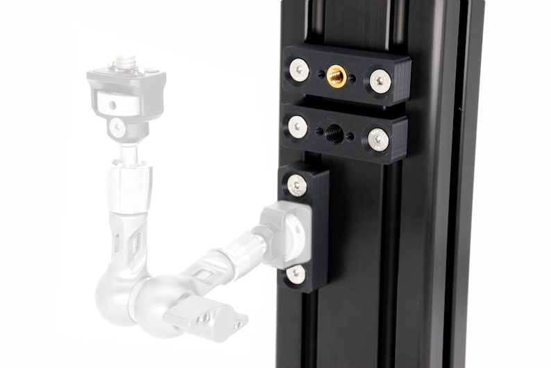 Puede incluir: Hardware de montaje de c&aacute;mara de metal negro con tornillos plateados y una inserci&oacute;n roscada dorada. El hardware est&aacute; fijado a un riel vertical negro, con un soporte de c&aacute;mara y un brazo articulado parcialmente visibles.