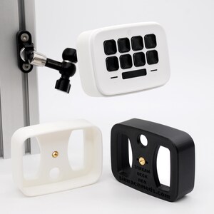May include: A white control deck with eight black buttons mounted on an adjustable black arm attached to a silver aluminum profile. Below are two empty rectangular frames, one white and one black, each featuring a central brass threaded insert.