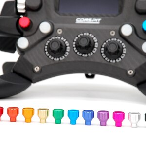 Peut inclure: Un volant de course noir avec le texte CORSPIT, dot&eacute; de plusieurs boutons et cadrans rotatifs. Sous le volant se trouvent onze petits boutons cylindriques stri&eacute;s dans un spectre de couleurs incluant rouge, orange, jaune, or, vert, bleu, violet, rose, blanc et noir.