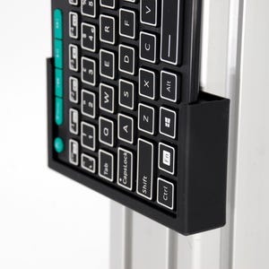 May include: A black keyboard with white keys is mounted on a silver metal support. The keyboard has a standard QWERTY layout with function keys and control keys. The keys are labeled with white letters and symbols.