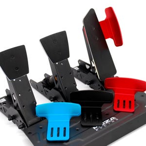 May include: Black and red racing pedals with a black base. The pedals have a rectangular design with a textured surface. The base has the text "MOZA RACING" printed on it. Additional colored components are blue and black.