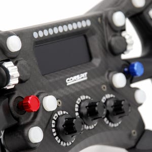 Peut inclure: Un volant de course en fibre de carbone noire avec un &eacute;cran num&eacute;rique central, le texte CORSPIT, plusieurs boutons-poussoirs blancs, trois molettes noires, un bouton rouge, un bouton bleu et une molette m&eacute;tallique argent&eacute;e sur le c&ocirc;t&eacute; gauche.