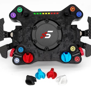 Può includere: Un volante da corsa nero con finitura in fibra di carbonio. Il volante ha diversi pulsanti e interruttori, tra cui un pulsante rosso, un pulsante blu e un pulsante giallo. Il volante ha anche un piccolo schermo con il numero "5" su di esso.