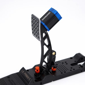 Könnte beinhalten: Ein schwarzes und silbernes Rennpedal mit blauem Akzent und dem Text "SIMSONN". Das Pedal hat eine perforierte Fußplatte und orangefarbene Einstellknöpfe. Die Basis ist schwarz und trägt den Text "LA PRIMA-S".