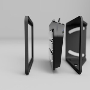 May include: A black, modular electronic device with a frame, a central unit with multiple compartments, and a back panel. The components are separated, suggesting assembly or customization. The design is modern and minimalist.