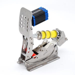 May include: A silver racing pedal with a perforated foot plate and a yellow spring. The pedal has a black and blue component with the text "SIMSONN". The design includes red and silver accents.