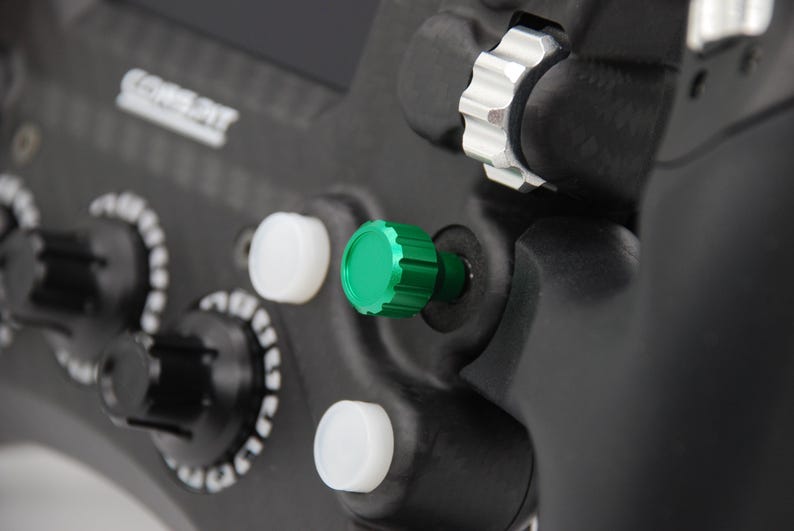 Peut inclure: Un volant de course noir dot&eacute; d'un bouton rotatif molet&eacute; vert, de deux boutons circulaires blancs et d'une molette m&eacute;tallique argent&eacute;e. L'appareil pr&eacute;sente des poign&eacute;es textur&eacute;es noires et le texte COREPIT imprim&eacute; en blanc sur le ch&acirc;ssis.