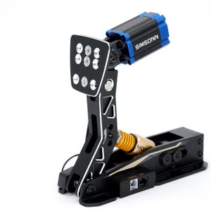 May include: A black and silver racing pedal with the brand name SIMSONN in blue. The pedal features a black base, a silver footpad with six circular holes, and a yellow and gold spring.