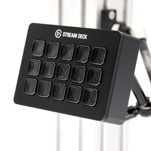 May include: Black Stream Deck with 15 square buttons. The device is mounted on a black and silver stand. The words "STREAM DECK" are printed in white on the top of the device.