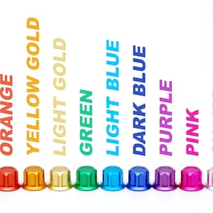 K&ouml;nnte beinhalten: Eine Reihe von elf kleinen, zylindrischen Metallkappen mit geriffelten Seiten in verschiedenen Farben: Rot, Orange, Gelbgold, Hellgold, Gr&uuml;n, Hellblau, Dunkelblau, Lila, Pink, Silber und Schwarz, wobei der Farbname jeweils dar&uuml;ber gedruckt ist.