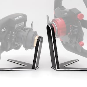 Op de afbeelding: Twee zwarte metalen standaards met zilveren randen ontworpen om racesturen vast te houden. Elke standaard heeft een brede, driepotige basis en een verticale steunarm die verbonden is met het midden van een stuurwiel, waaronder één met Fanatec-label.