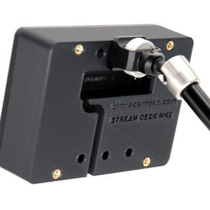 May include: A black Stream Deck MK2 device with a mounting arm. The device has gold-colored screws and the text "slmracemods.com" and "STREAM DECK MK2" printed on it. The mounting arm is black and silver.