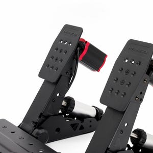 May include: A black racing pedal set featuring two upright pedals with the MOZA logo embossed at the top. Each pedal has a textured face with multiple circular cutouts, a red cylindrical component at the rear, and a silver shock absorber mechanism.