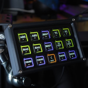 Könnte beinhalten: Ein schwarzes Bedienfeld mit beleuchteten Tasten, die mit Abkürzungen wie ABS, BIAS und MAP beschriftet sind. Die Tasten haben verschiedene Farben, darunter Grün, Blau und Orange. Das Panel ist an einer Metallhalterung befestigt.