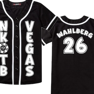 May include: Black baseball jersey with white accents. The front features the text "N.K.O.T.B. VEGAS" in white block letters, with a casino chip graphic. The back displays "WAHLBERG 26" in white. A button-down, short-sleeved shirt.
