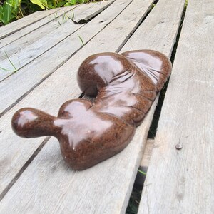 May include: A smooth, dark brown, abstract sculpture made of stone, resting on a wooden surface.