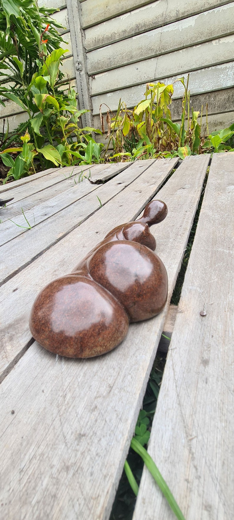 May include: A smooth, brown, abstract sculpture made of stone, resting on a wooden surface.