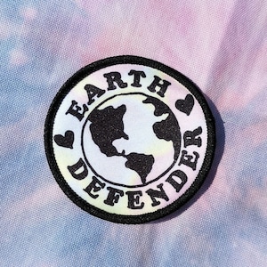 May include: A round patch with the words "EARTH DEFENDER" encircling a black and white world map. Two small hearts flank the map. The patch is on a tie-dye background of blue, pink, and yellow.