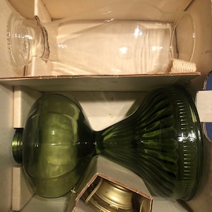 May include: A set of two glass oil lamps in a cardboard box. The larger lamp is green glass with a fluted design. The smaller lamp is clear glass. The lamps are packaged with a metal wick holder.
